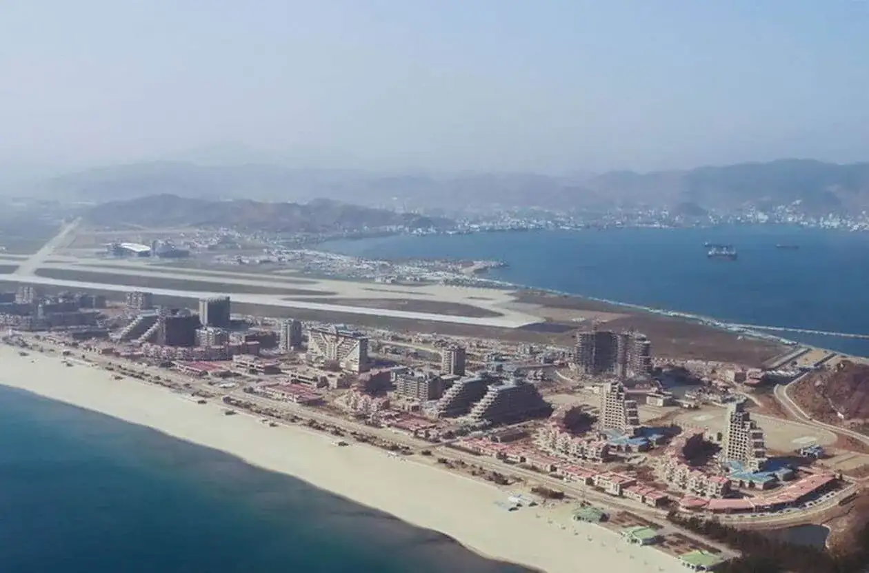 Vue aérienne d'une station balnéaire en construction en Corée du Nord, avec des bâtiments modernes, une plage et un aéroport.