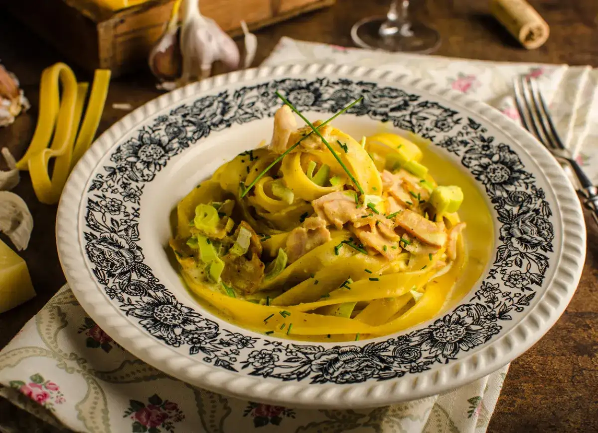 Talerz z makaronem tagliatelle w kremowym sosie z kawałkami mięsa i szczypiorkiem.