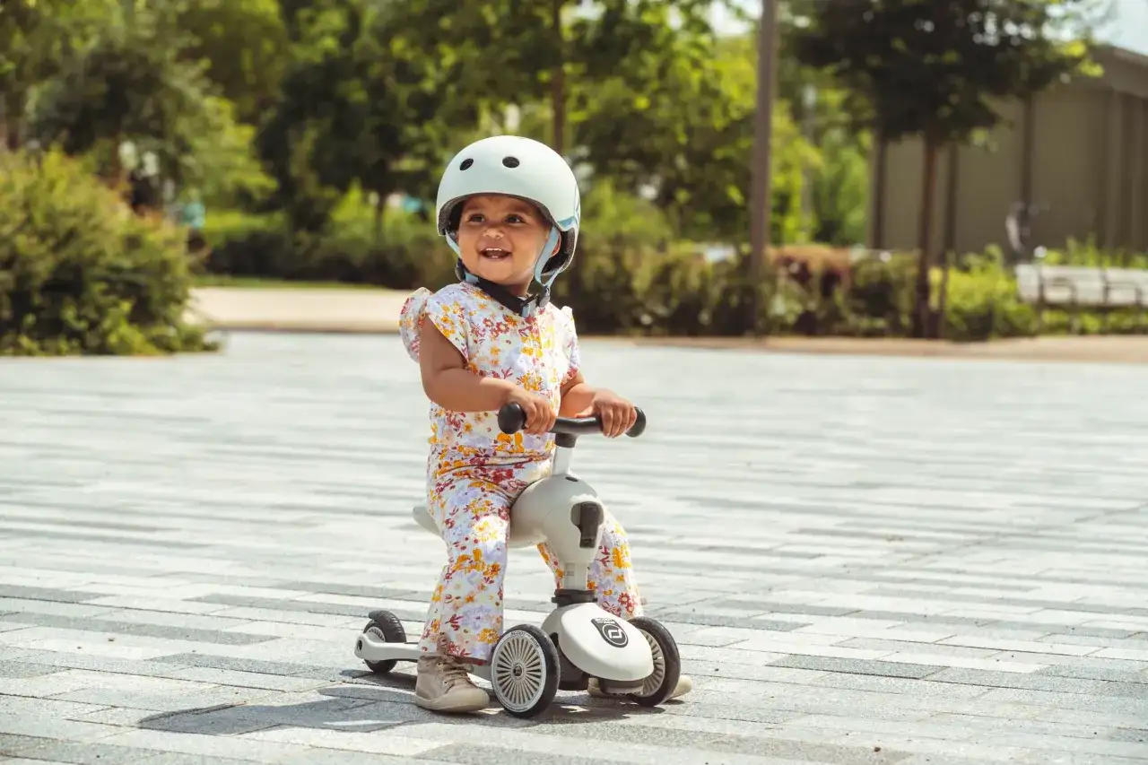 Uśmiechnięte dziecko w kasku na jeździku Scoot and Ride od kiedy zaczęło swoją przygodę z jazdą.