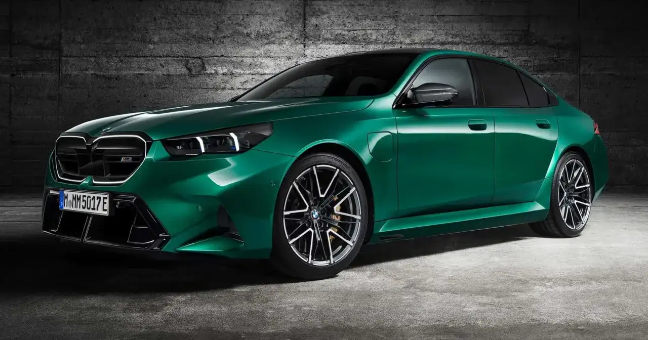 Zielony BMW M5 Competition z nowoczesnymi światłami i felgami stoi na tle betonowej ściany.