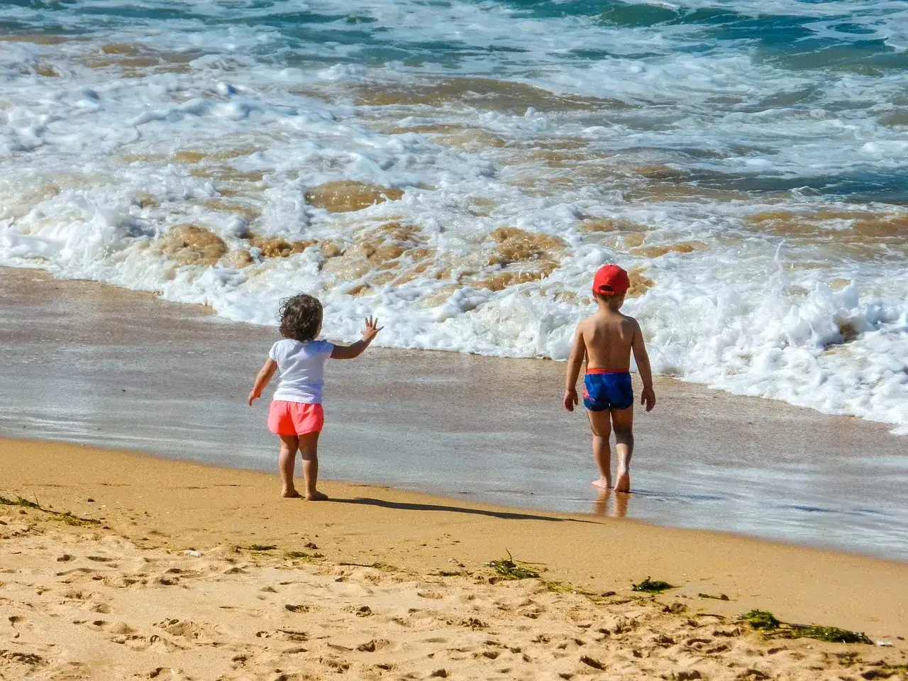 Dzieci w strojach kąpielowych dwuczęściowych dla dzieci bawią się na plaży, machając do fal.