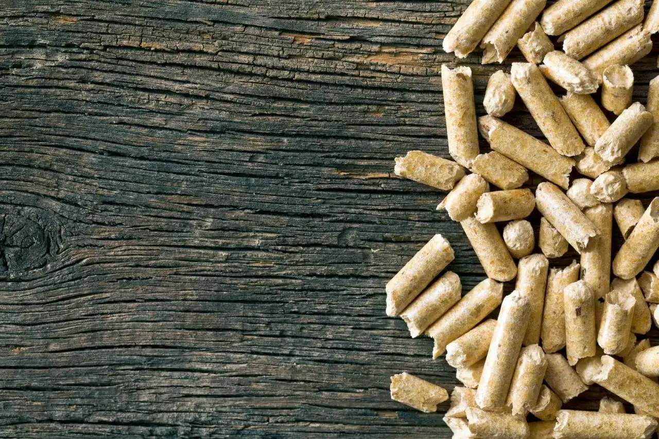 Drewniane deski i stos pelletu. Czy pellet jest ekologiczny? To pytanie zadaje sobie wielu, a ten obrazek pokazuje jego naturalne pochodzenie.