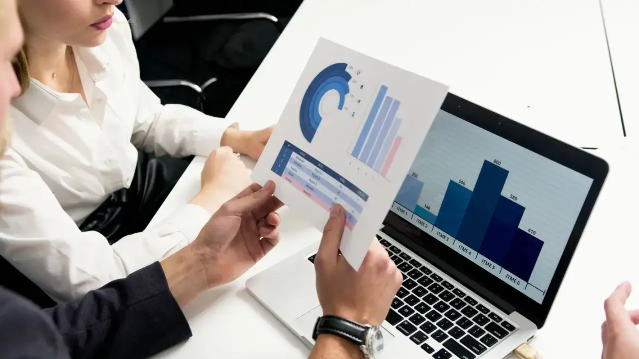Data scientist analizuje wykresy i dane na laptopie, omawiając wyniki z kolegą.