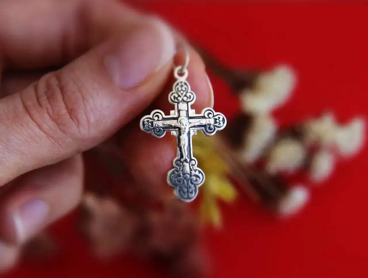 Srebrny krzyż prawosławny w dłoni. Różnice między prawosławiem a katolicyzmem mogą być widoczne w symbolice.