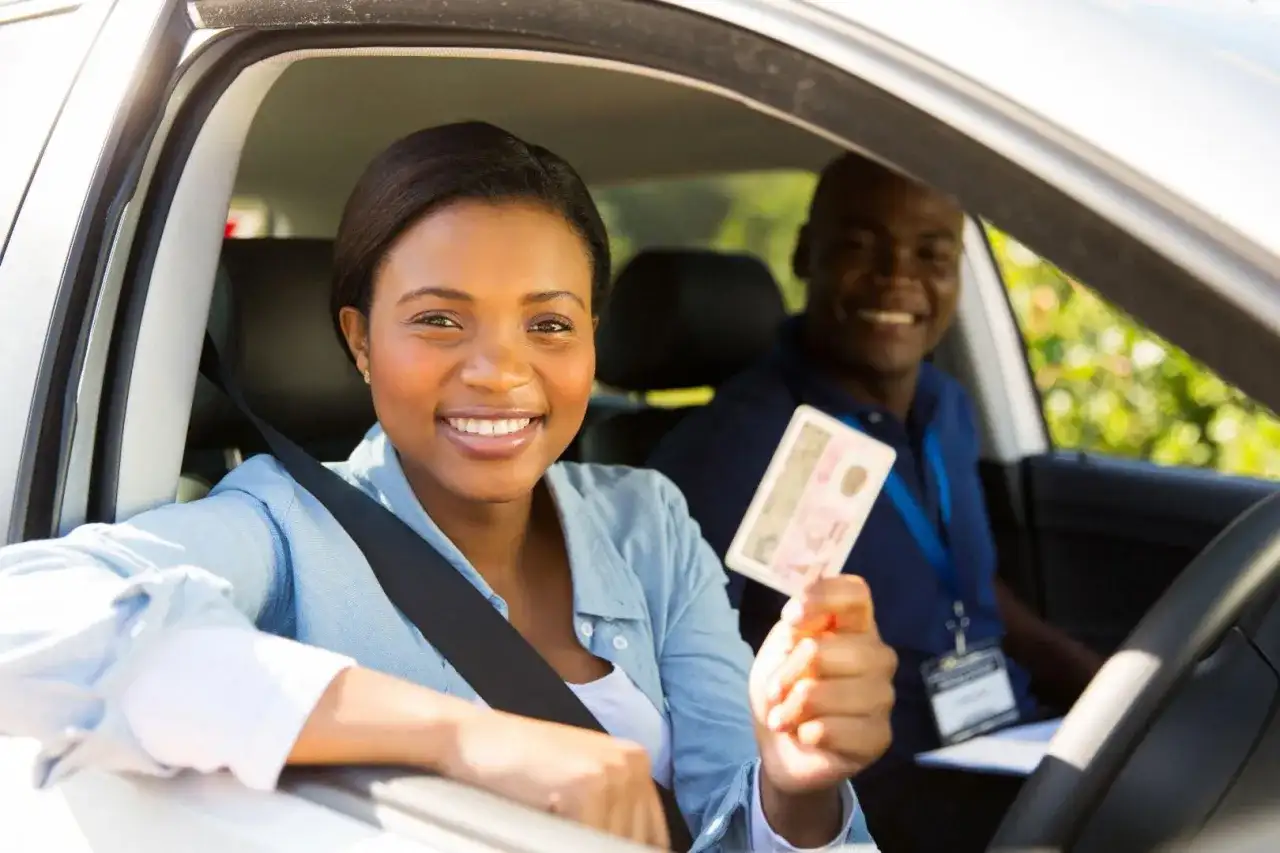 Une jeune femme souriante tient son permis de conduire, fière de sa réussite. L'auto-école veille à la répression des fraudes pour des formations honnêtes.