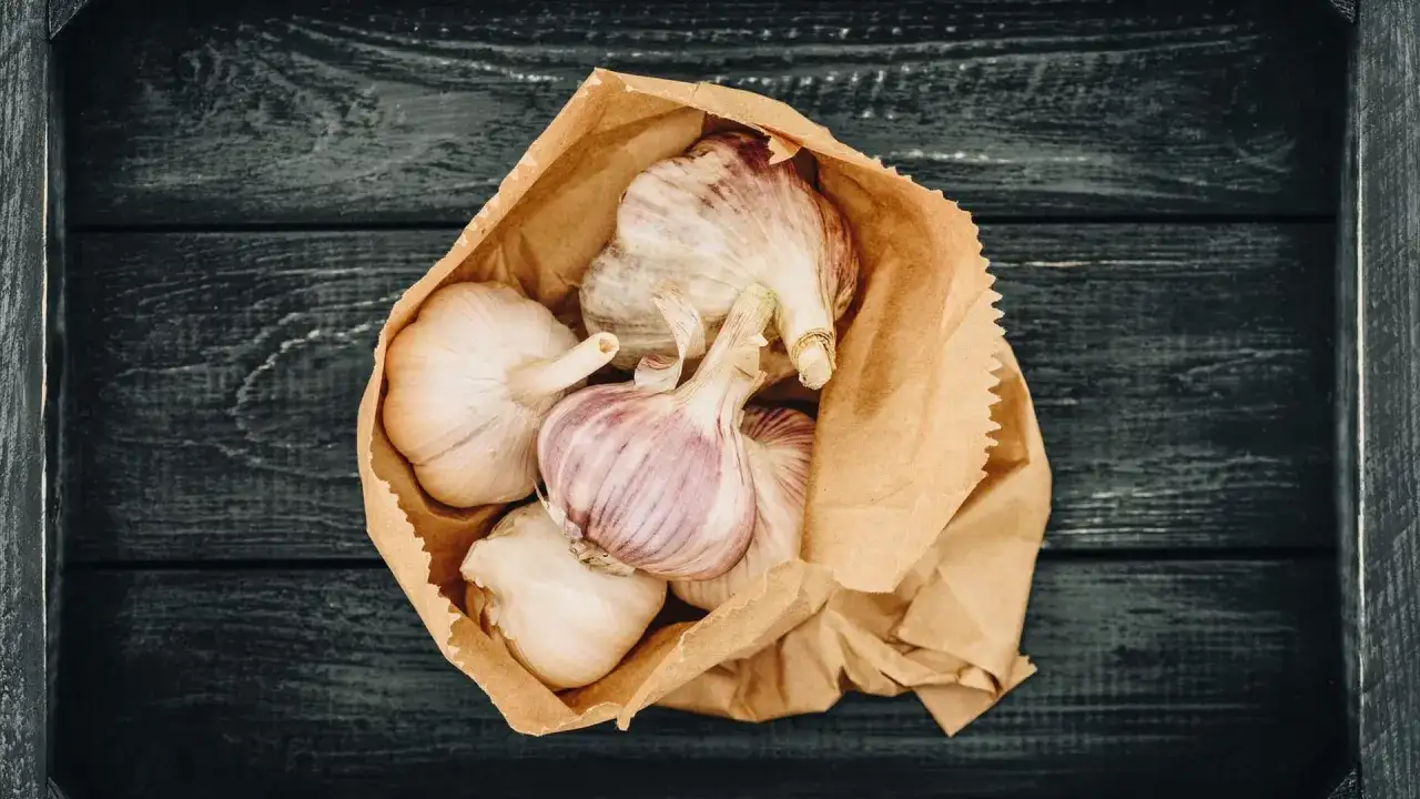 Frische Knoblauchzehen in einer Papiertüte, bereit zum **knoblauch lagern** auf dunklem Holz.