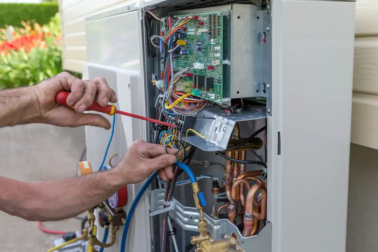 Fachowiec wykonuje serwis pomp ciepła Hitachi, pracując przy otwartej jednostce zewnętrznej z widoczną elektroniką i przewodami.