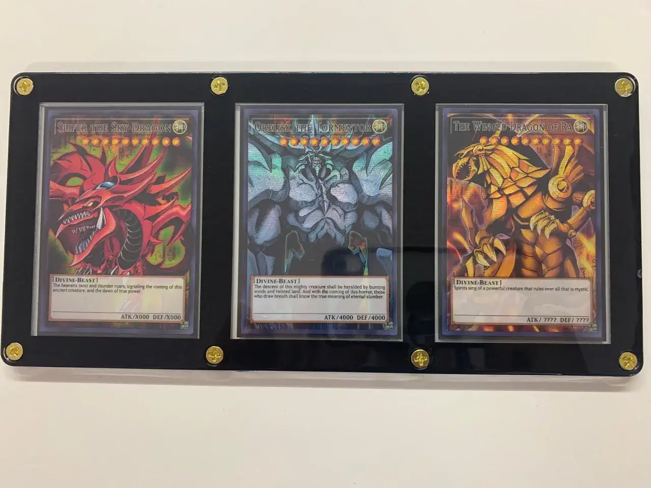 Trzy karty Yu-Gi-Oh! w ramce: Slifer the Sky Dragon, Obelisk the Tormentor i The Winged Dragon of Ra.