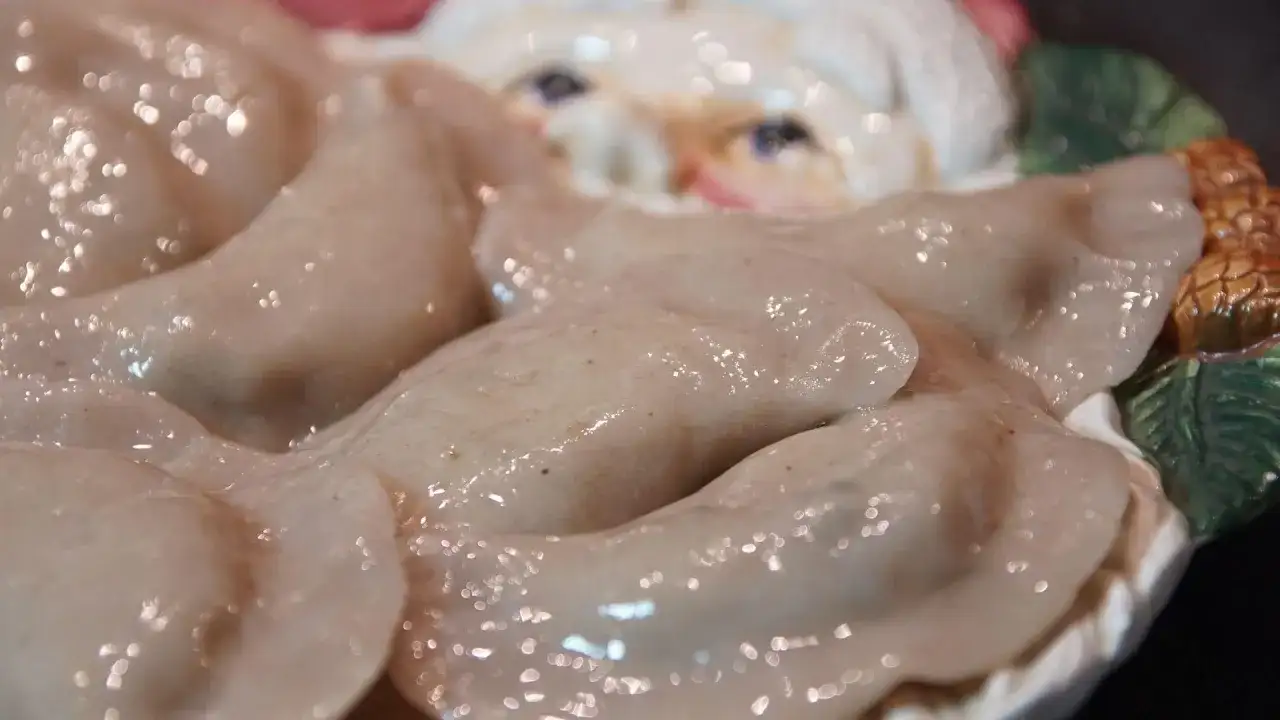 Świeżo ugotowane pierogi, błyszczące od wody, leżą na talerzu z motywem Mikołaja. Idealne, by dowiedzieć się, jak gotować pierogi.