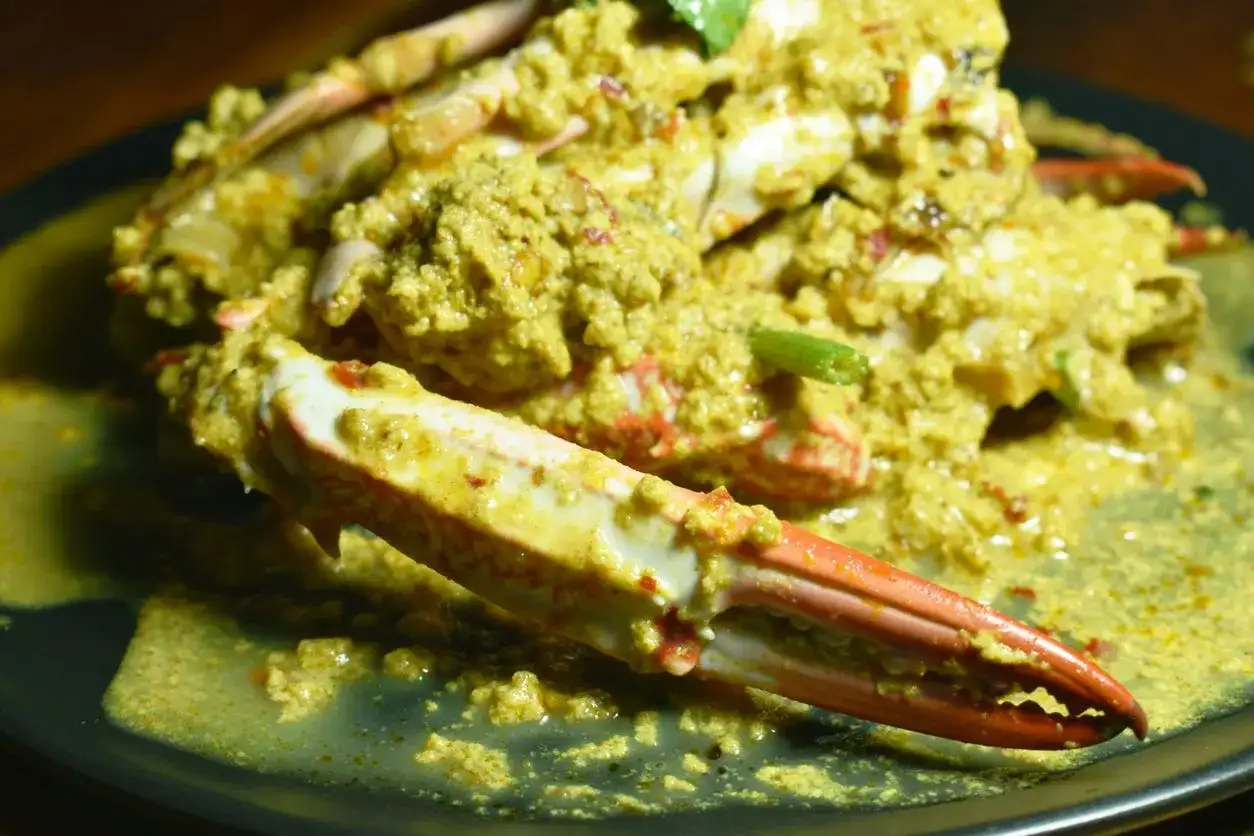 Krab w żółtym sosie curry na czarnym talerzu.