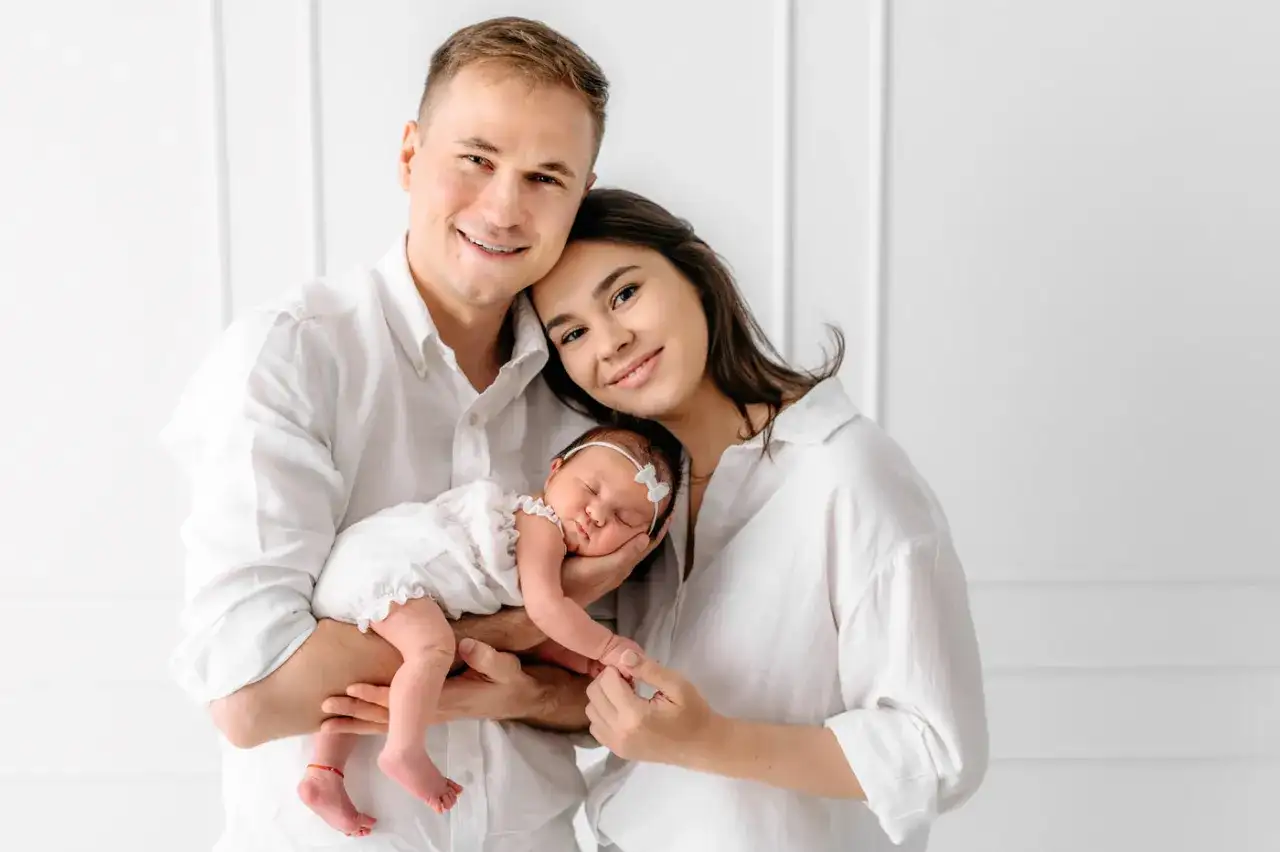 Szczęśliwa rodzina z noworodkiem w białych ubraniach, pozująca do sesji zdjęciowej.