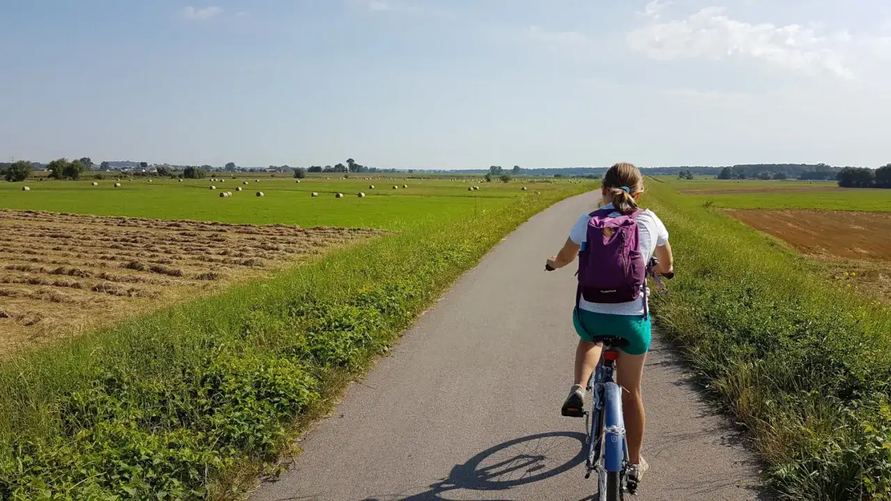 Dziewczynka na rowerze przemierza malowniczą wiślaną trasę rowerową Niepołomice, mijając pola z sianem i zielone łąki.