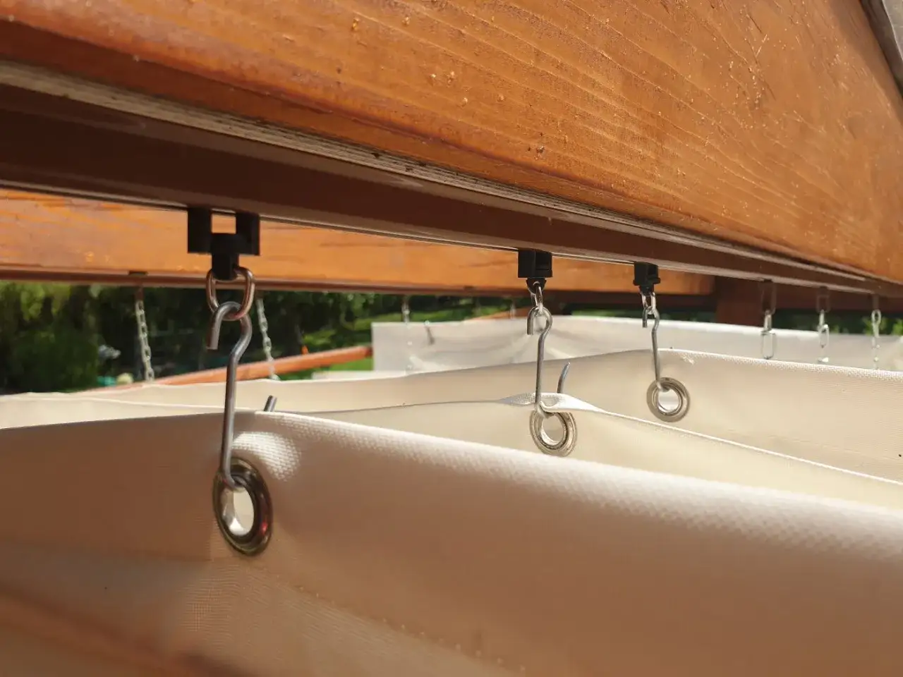 System mocowania rolety rzymskiej poziomej DIY. Metalowe haczyki łączą tkaninę z szyną pod drewnianą belką.