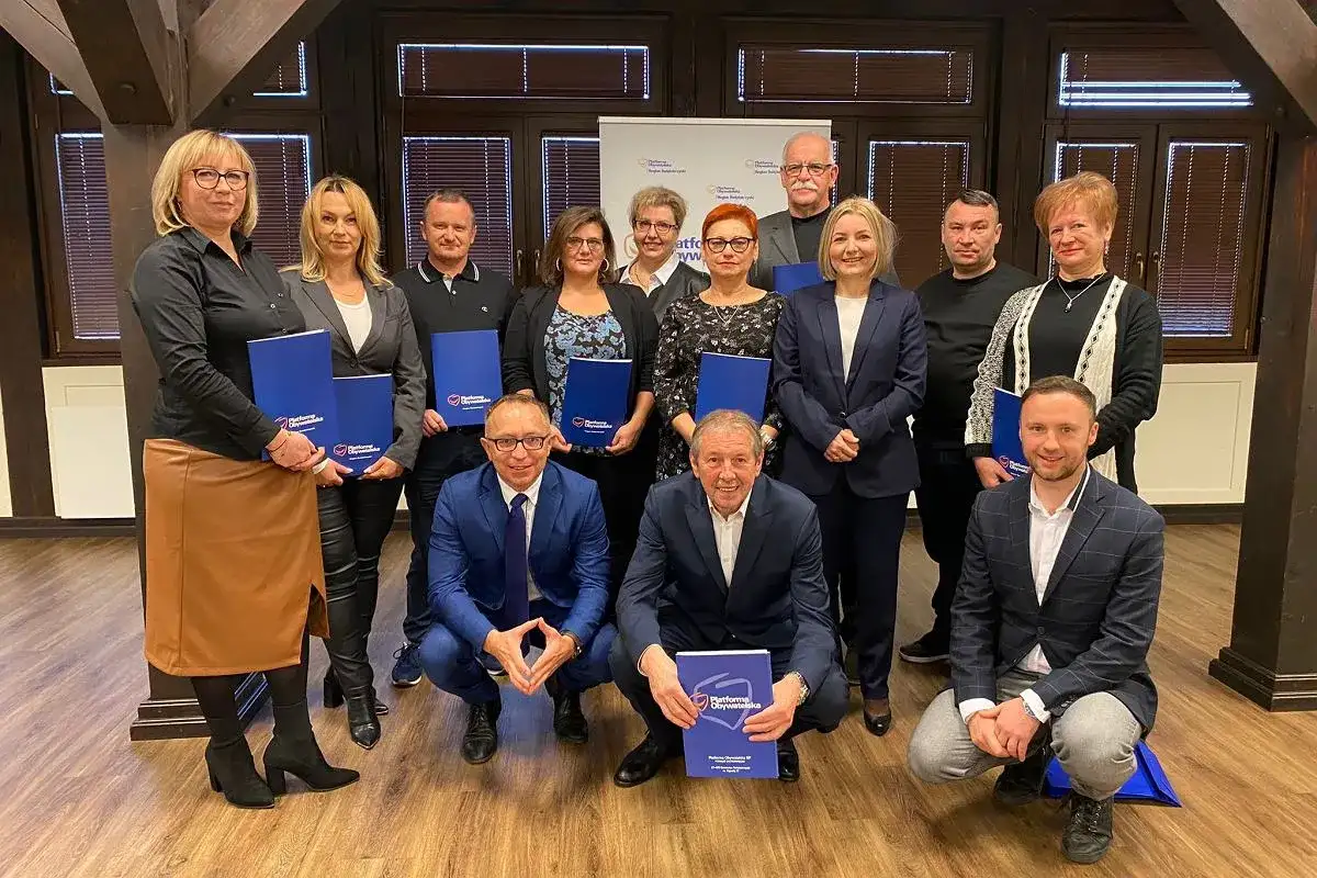 Grupa osób pozuje do zdjęcia z niebieskimi folderami. Na folderach widnieje napis "Platforma Obywatelska".