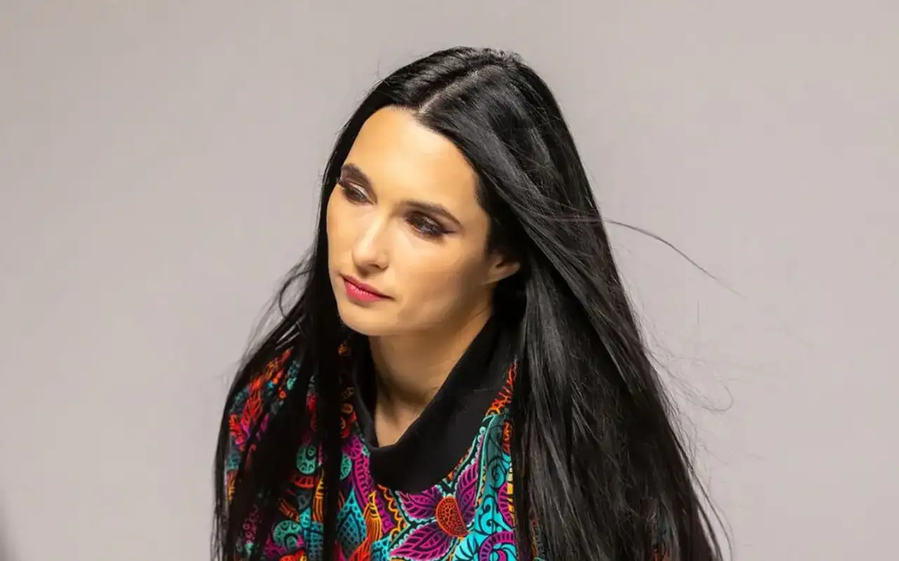 Portret kobiety z długimi, czarnymi włosami, w kolorowej bluzce. Emilia Sanecka, data urodzenia nieznana, patrzy w bok.
