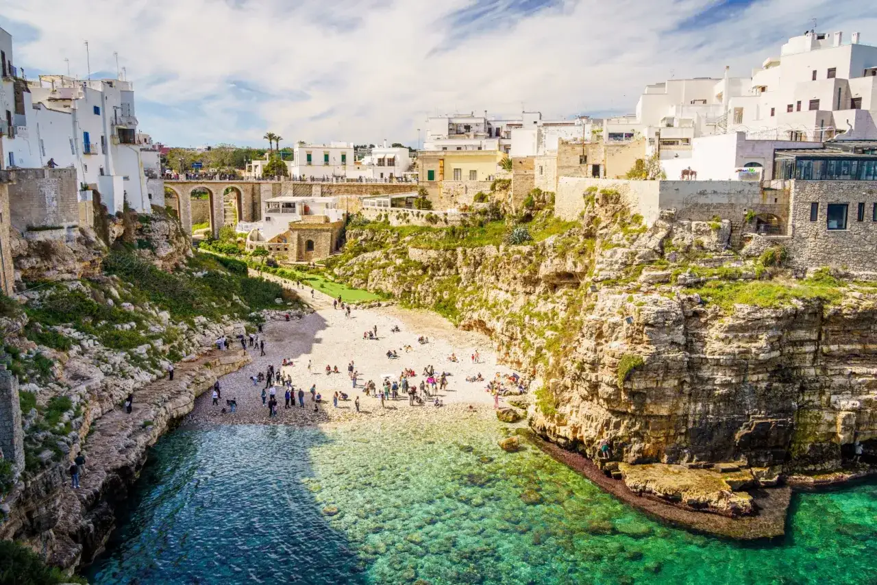 Malownicze klify i białe domy Polignano a Mare, z plażą pełną ludzi i turkusową wodą.