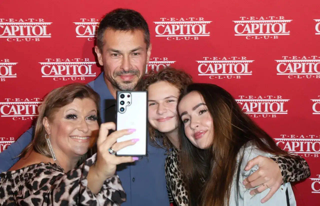 Katarzyna Skrzynecka z rodziną robi selfie. Uśmiechnięci rodzice i ich dzieci pozują na tle czerwonego banera z napisem "Teatr Capitol".