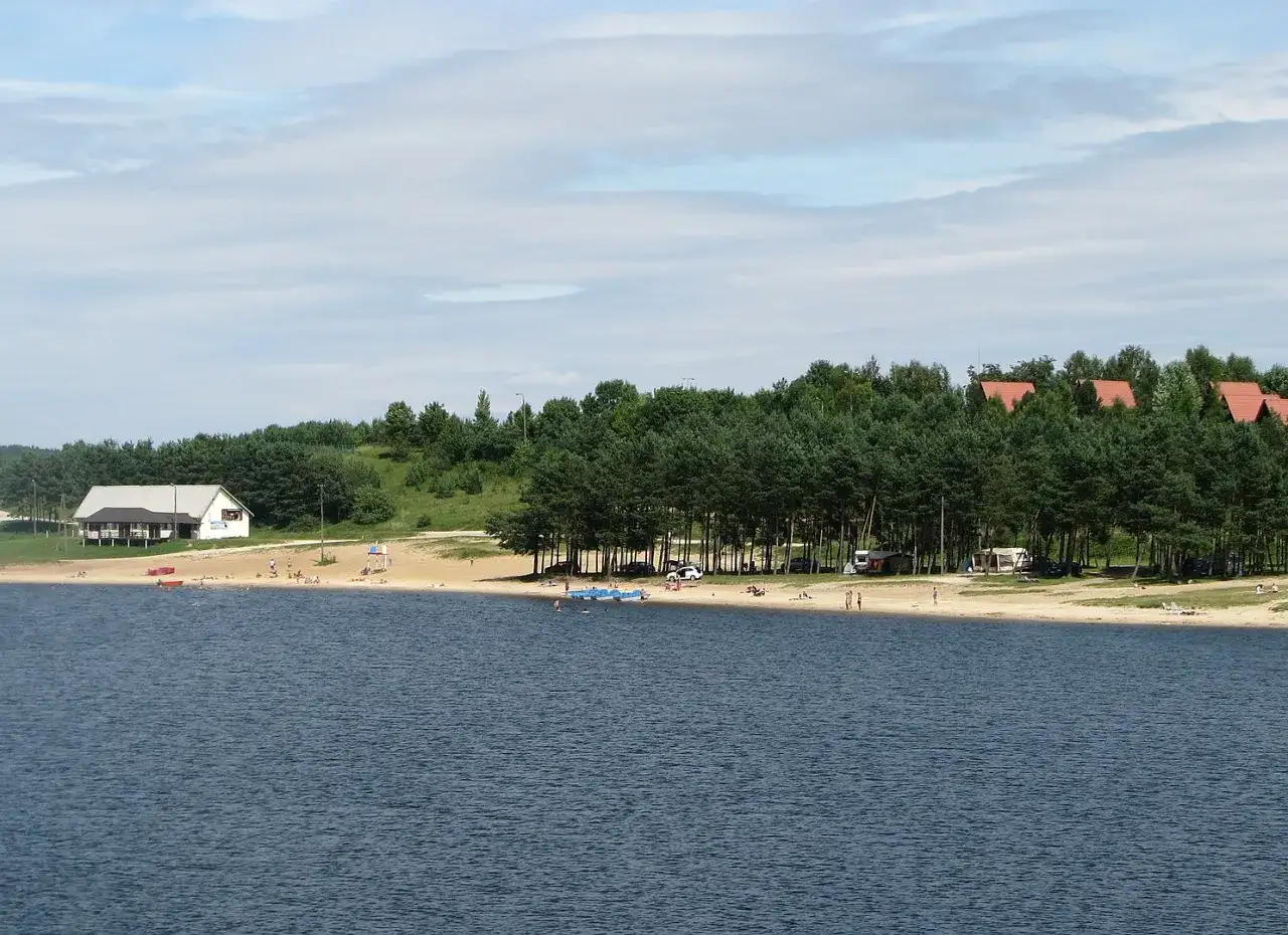 Słoneczny dzień nad zalewem Chańcza. Plaża z ludźmi, domki letniskowe i las.