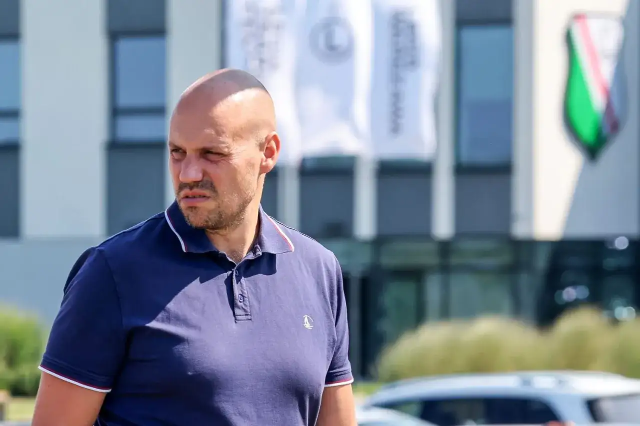 Łysy mężczyzna w granatowej koszulce polo, dyrektor sportowy Legii, patrzy w bok.