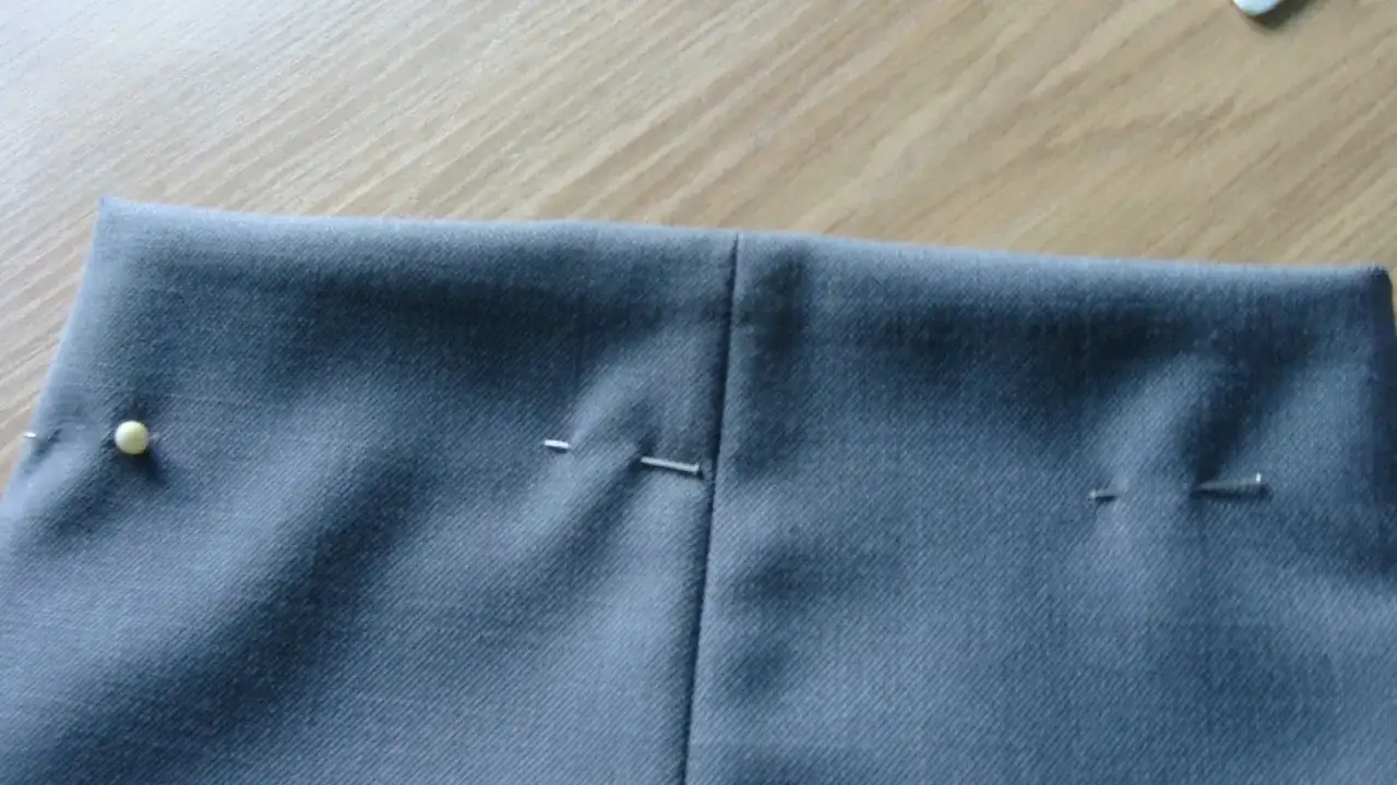 Szare spodnie z zaznaczonymi zaszewkami, gotowe do szycia. Szpilki trzymają materiał.