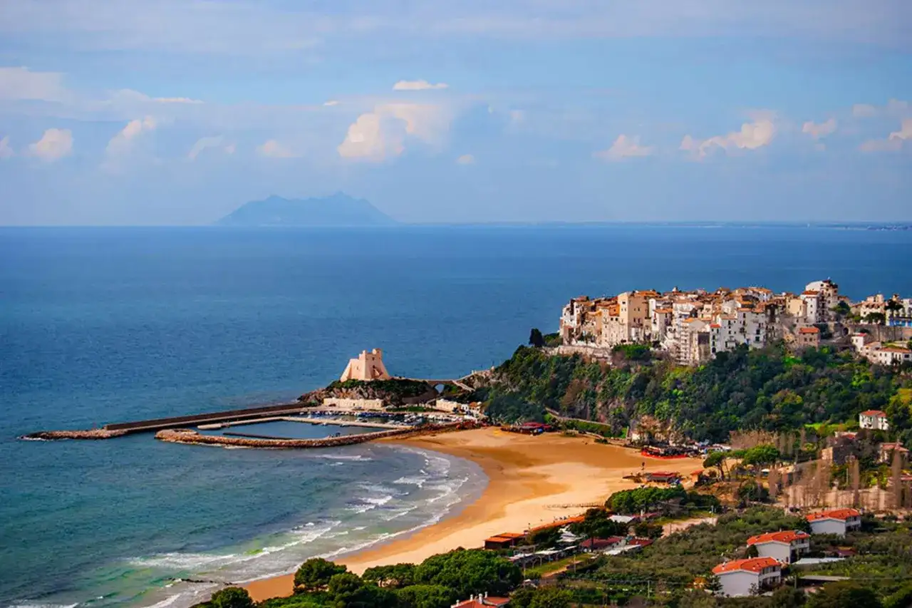 Vue d'une ville côtière italienne perchée sur une falaise, avec une plage et un port en contrebas.