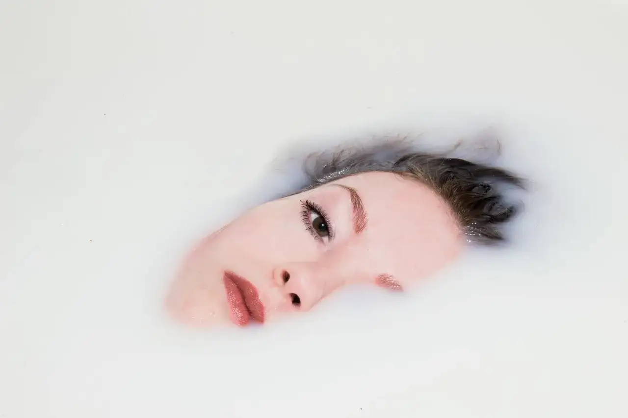 Rostro de mujer sumergido en leche, parte de un ritual de doble limpieza para una piel radiante.