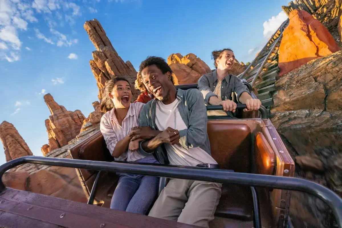 Radość na rollercoasterze w europejskim Disneylandzie. Grupa przyjaciół krzyczy z ekscytacji, przeżywając przygodę wśród skalistych krajobrazów.