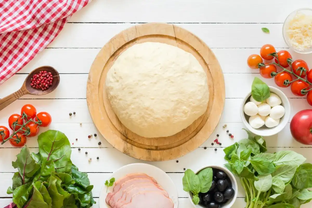 Świeże ciasto na pizzę, pomidorki, mozzarella, oliwki i bazylia. Idealne składniki do przygotowania pysznej pizzy. Dowiedz się, jak przechować ciasto na pizze, by było zawsze gotowe.