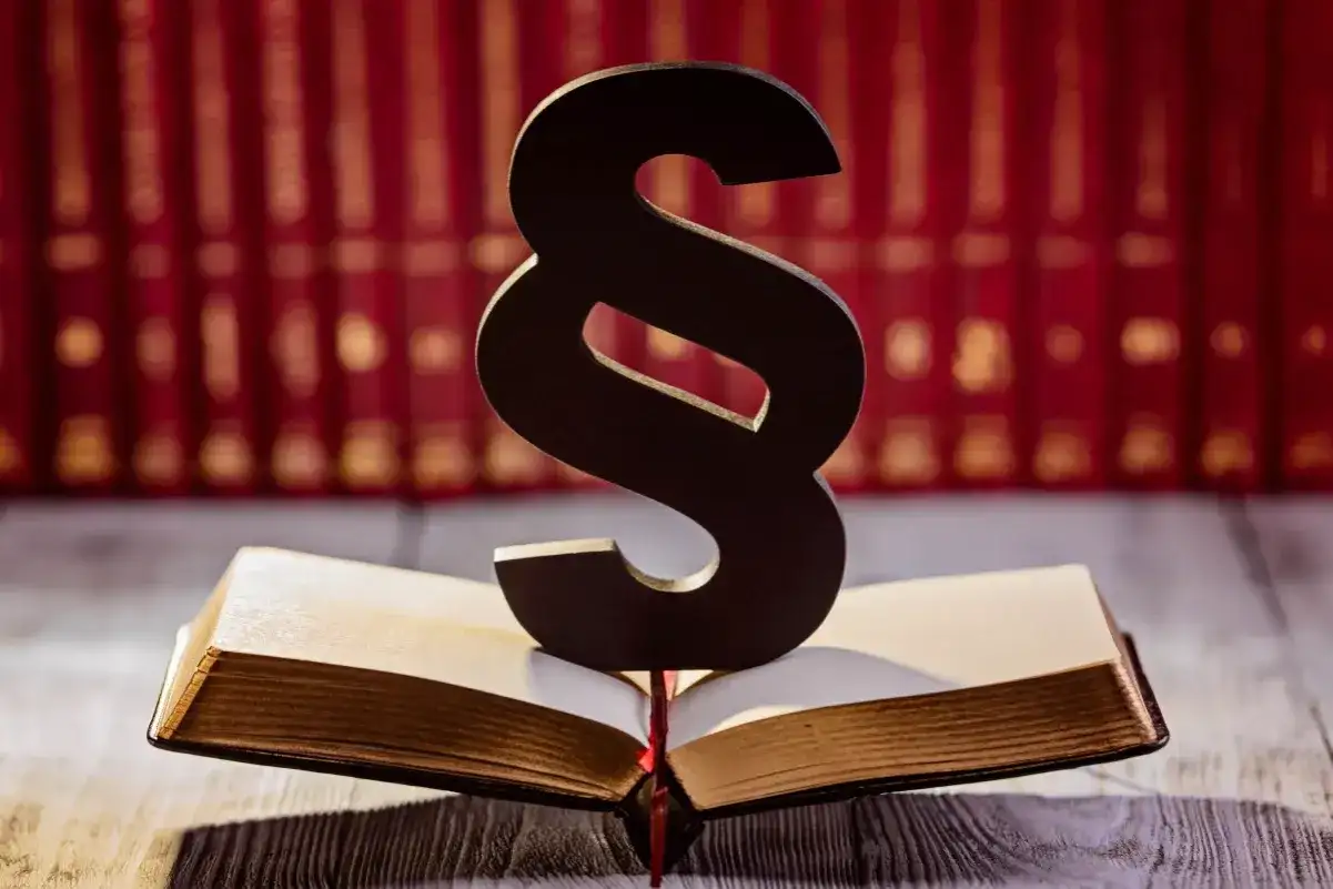 Symbol paragrafu na otwartej księdze, w tle rząd czerwonych ksiąg. Symbolizuje prawo i sprawiedliwość, a może nawet nadzieję na amnestia.
