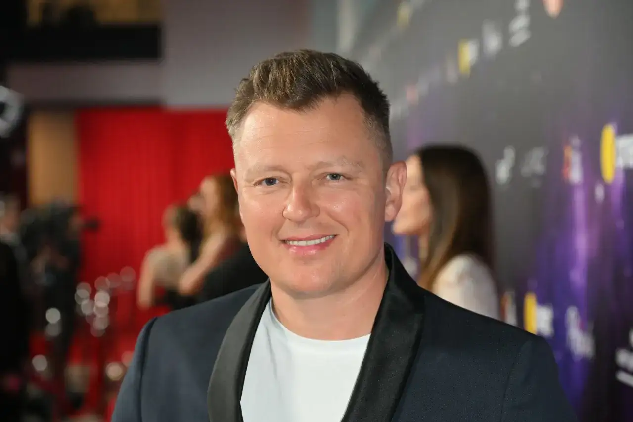Uśmiechnięty Rafał Brzozowski na ściance. Wiele osób zastanawia się, ile lat ma Rafał Brzozowski, ale na zdjęciu tego nie widać.