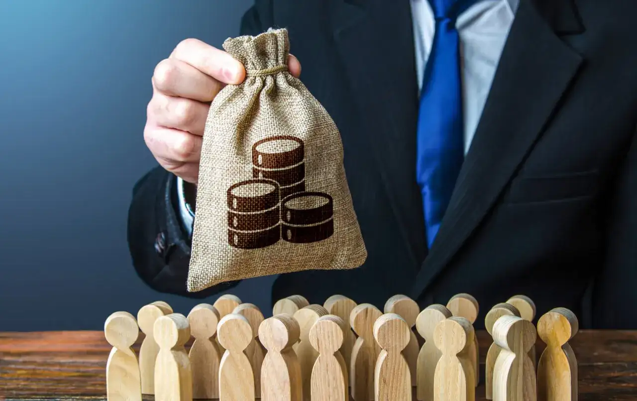 Hr manager w garniturze trzyma worek z pieniędzmi nad grupą drewnianych ludzików.