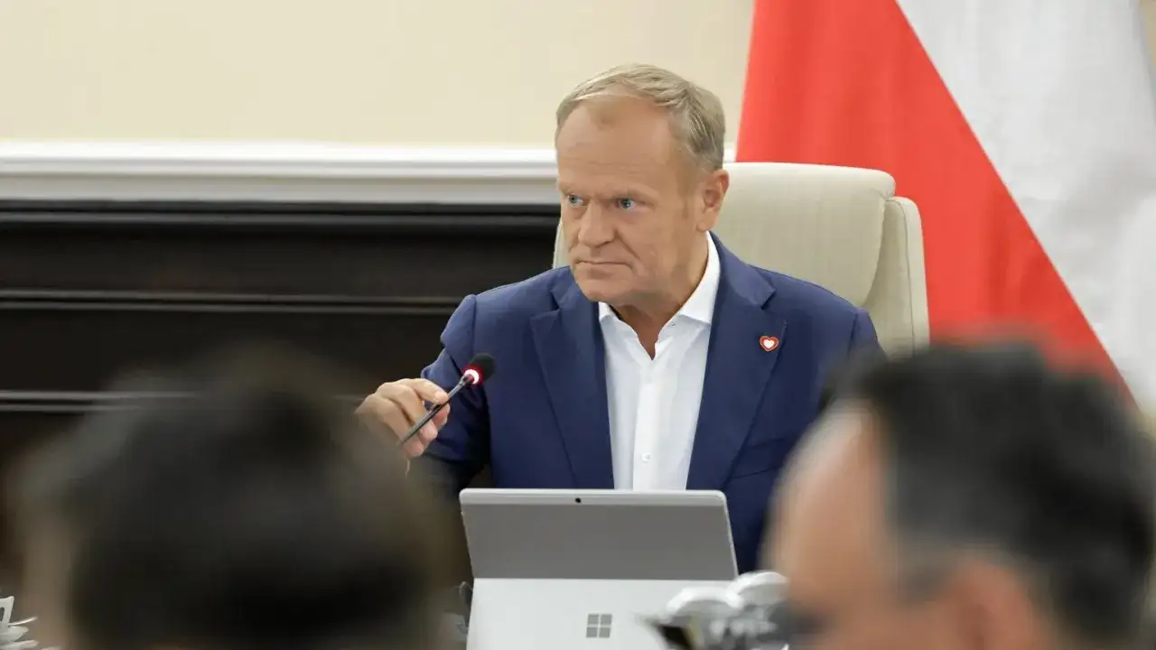 Donald Tusk w Płocku podczas spotkania. Siedzi przy stole z mikrofonem i laptopem.