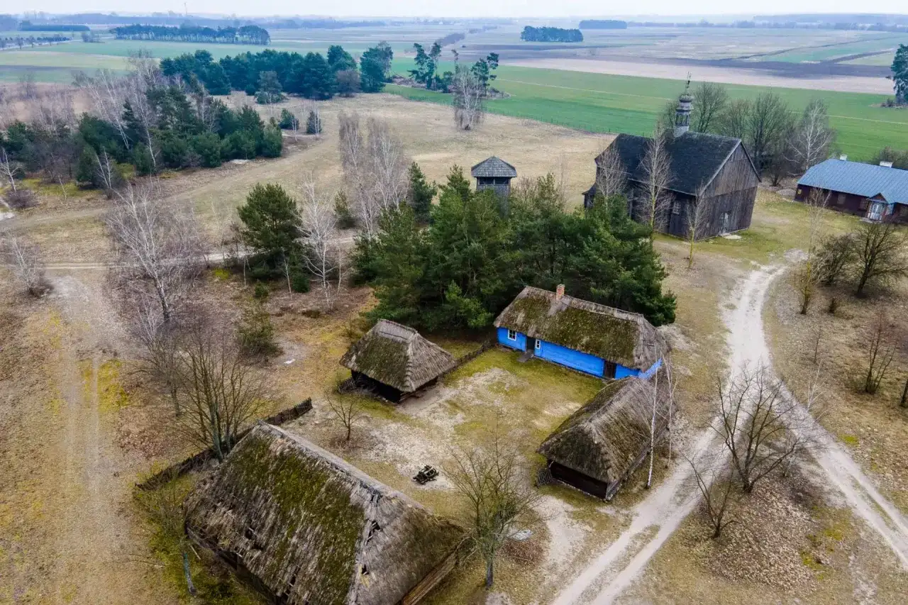 Skansen wsi łowickiej z drewnianymi chatami, kościołem i wieżą.