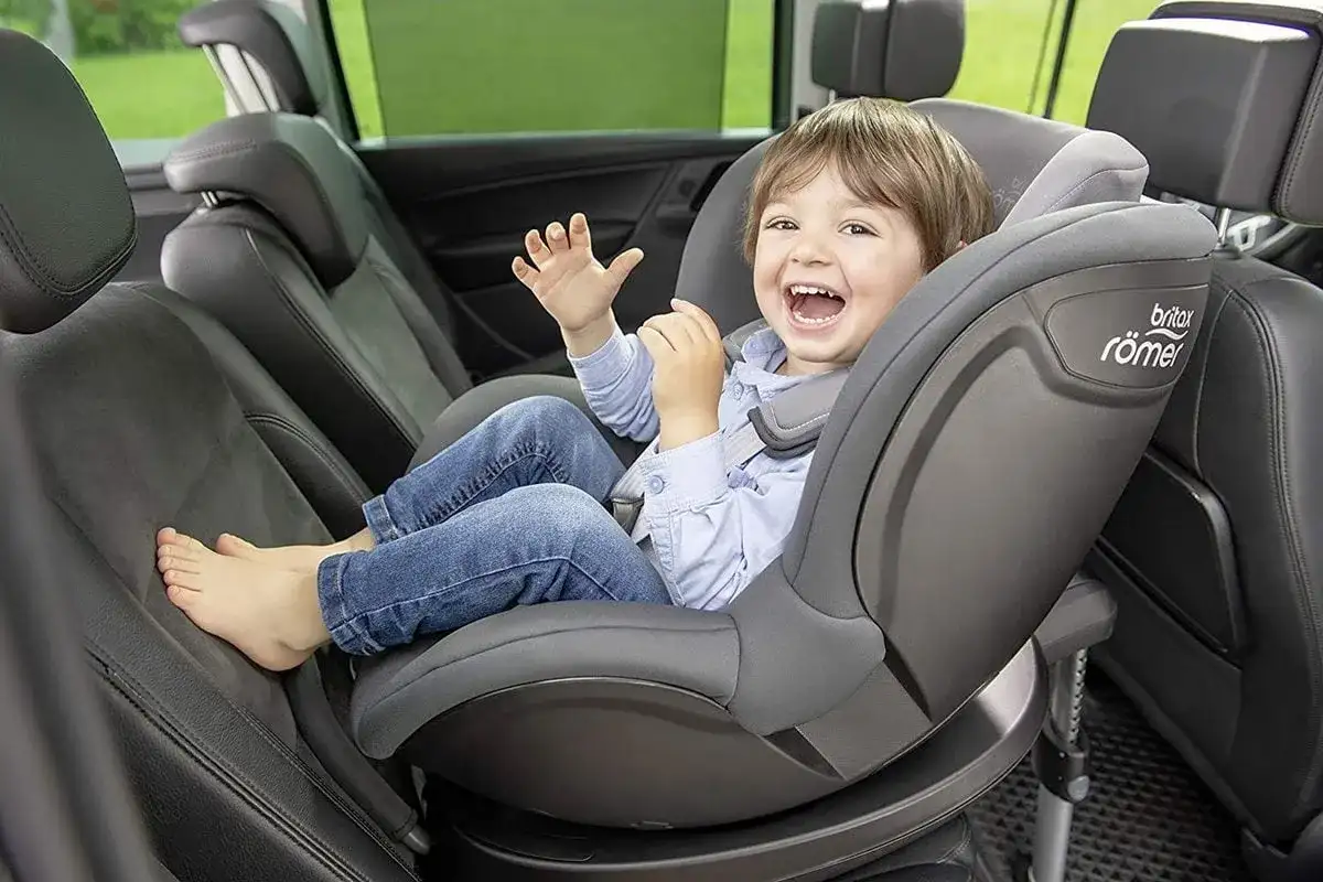 Uśmiechnięty chłopiec w foteliku samochodowym Britax Römer.