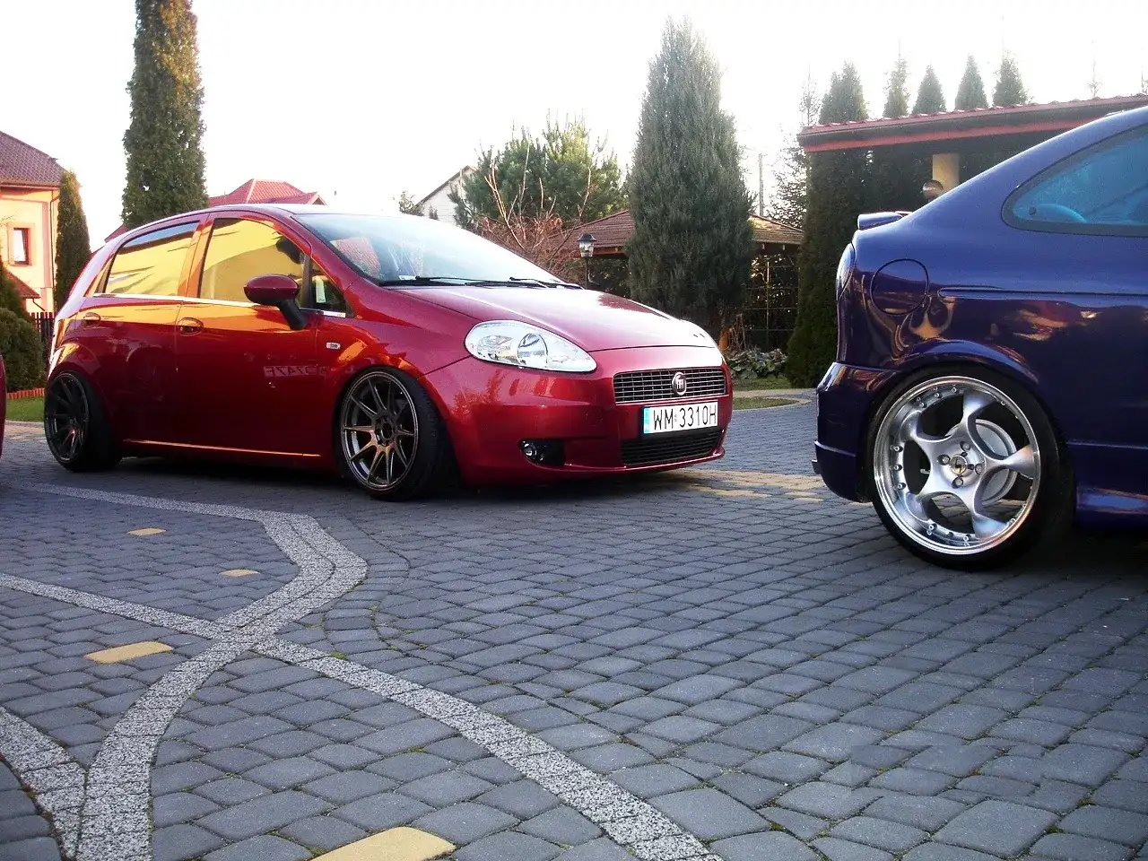 Czerwony Fiat Grande Punto 1.4 z przyciemnianymi szybami i sportowymi felgami, obok niebieski samochód. Rozmiar opon dopasowany do modyfikacji.