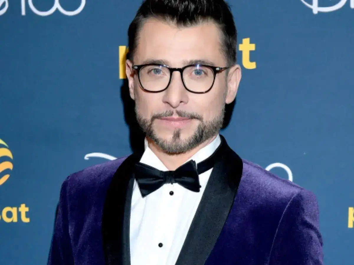 Kacper Kuszewski w fioletowym aksamitnym smokingu z czarną muszką. Wygląda elegancko, jakby wybierał się na galę, gdzie może spotkać swoją żonę.