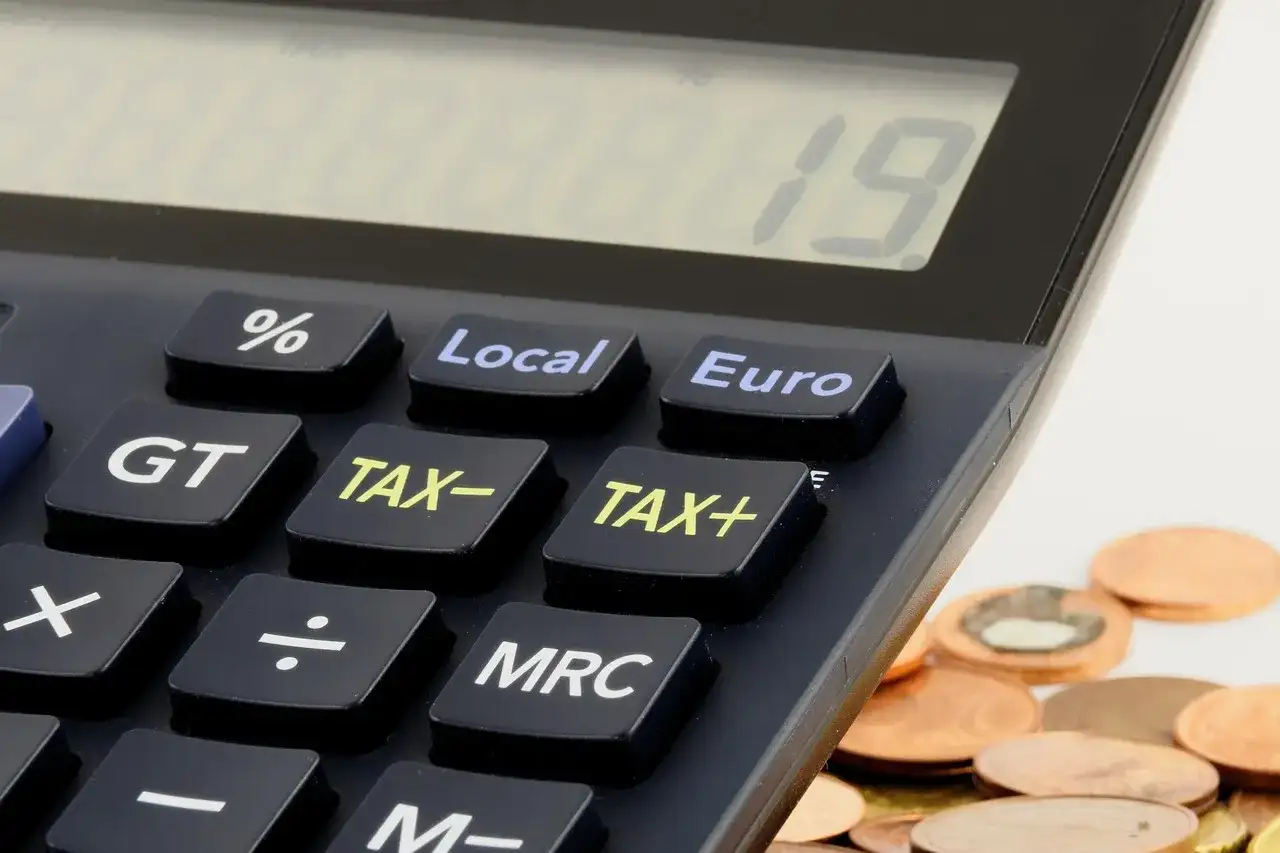 Kalkulator z klawiszami "TAX+", "TAX-" i "Euro" obok stosu monet. Czas na rozliczenie działalności gospodarczej do kiedy?