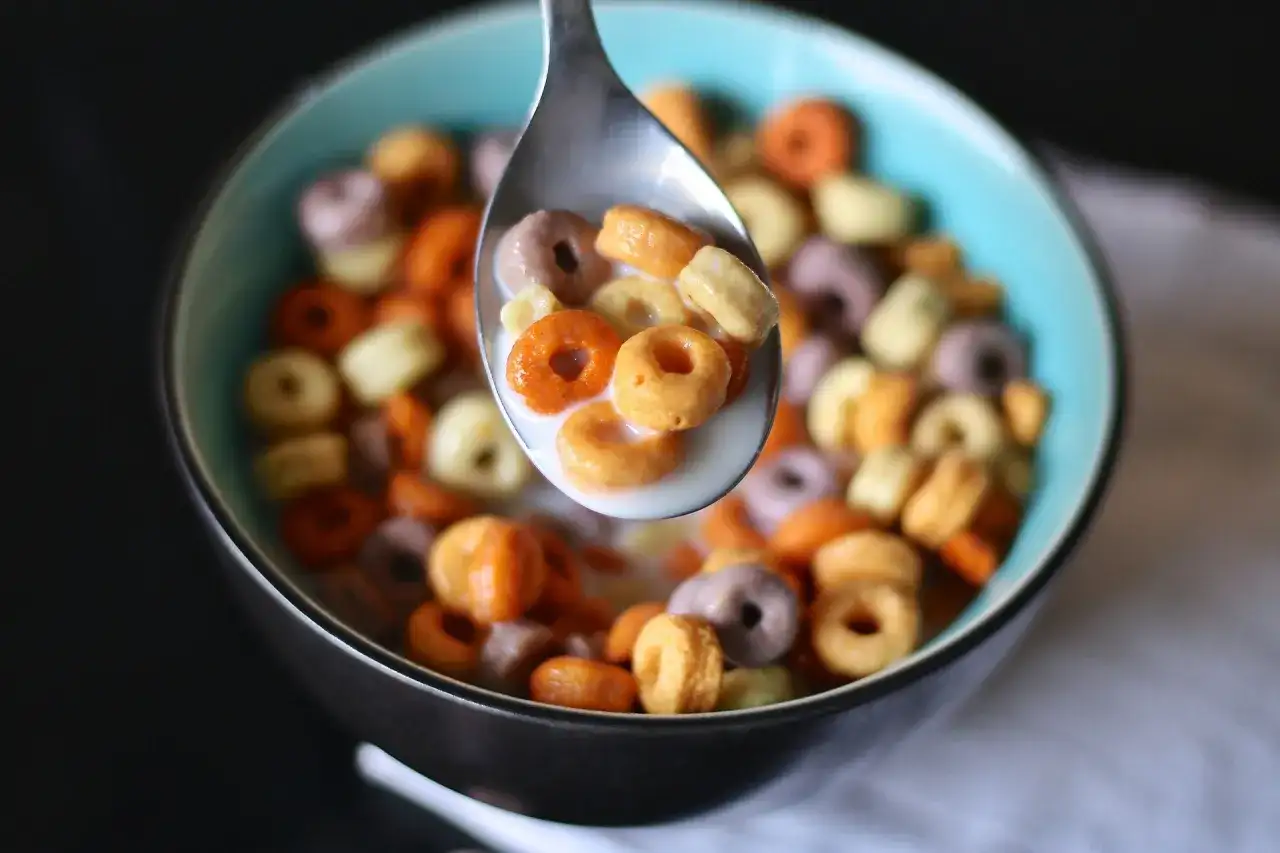 Kolorowe kółeczka płatków śniadaniowych w mleku, nabierane łyżką. Pyszny, kolorowy cereal po polsku na śniadanie.