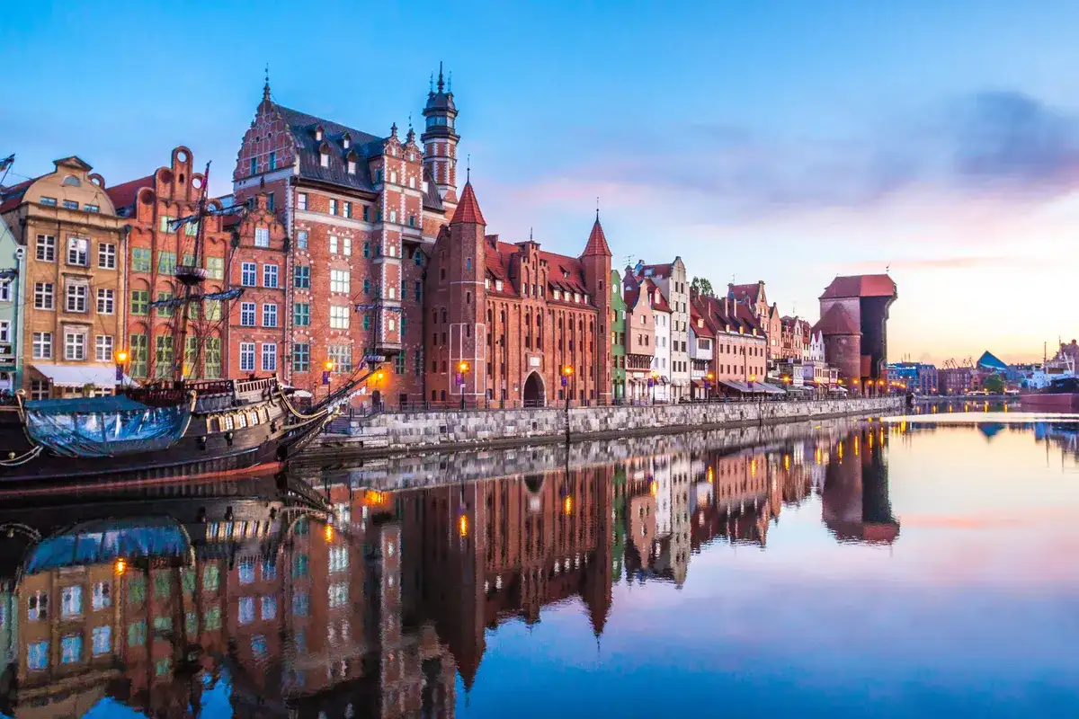Zachód słońca nad Motławą w Gdańsku, z zabytkowymi kamieniczkami i żaglowcem. Idealne miejsce na podróż, gdy planujesz loty Wrocław Gdańsk.