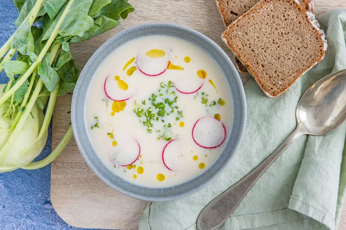 Cremige Kohlrabisuppe low carb, garniert mit Radieschenscheiben und Kresse. Dazu Vollkornbrot und ein Löffel.