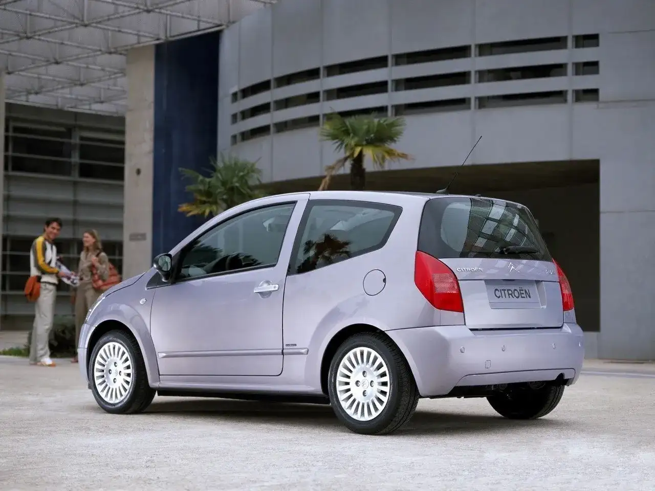 Jasnoszary Citroën C2 z parą na tle nowoczesnego budynku.