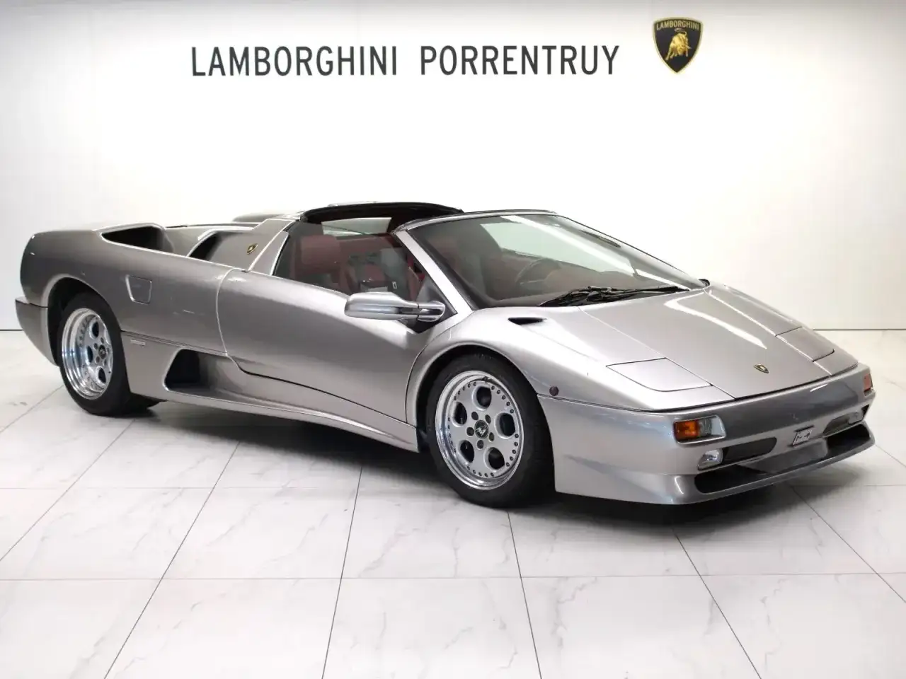 Srebrny kabriolet Lamborghini Diablo z czerwonym wnętrzem, zaparkowany na białej, marmurowej podłodze.