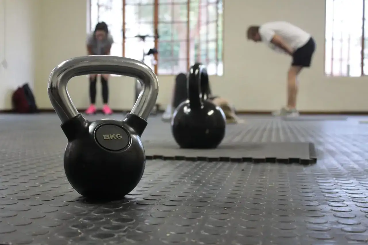 Kettlebell 8kg na siłowni, w tle ćwiczący ludzie.