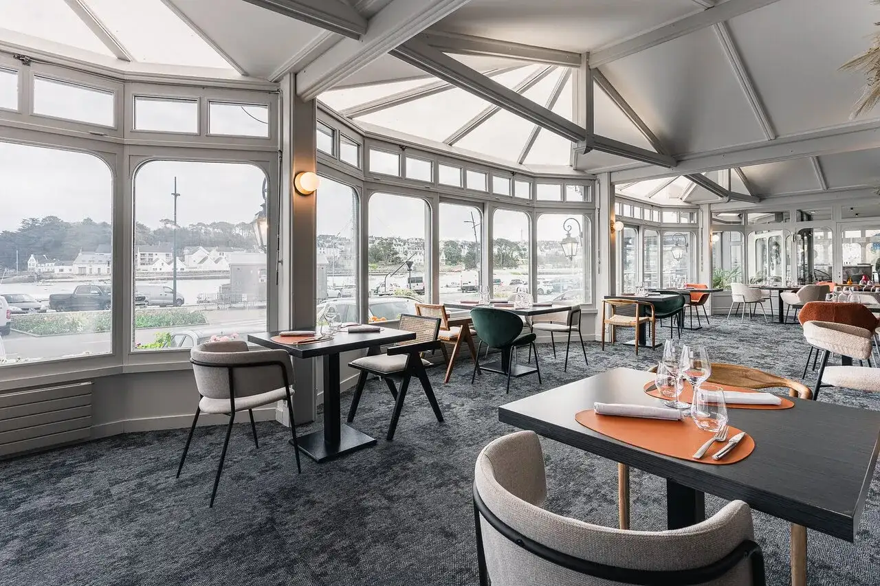 Salle de restaurant lumineuse avec vue sur le port, tables dressées et chaises modernes.