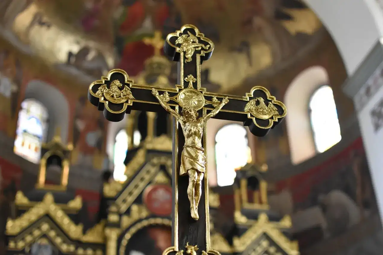 Złoty krzyż z postacią Jezusa na ciemnym tle kościoła.