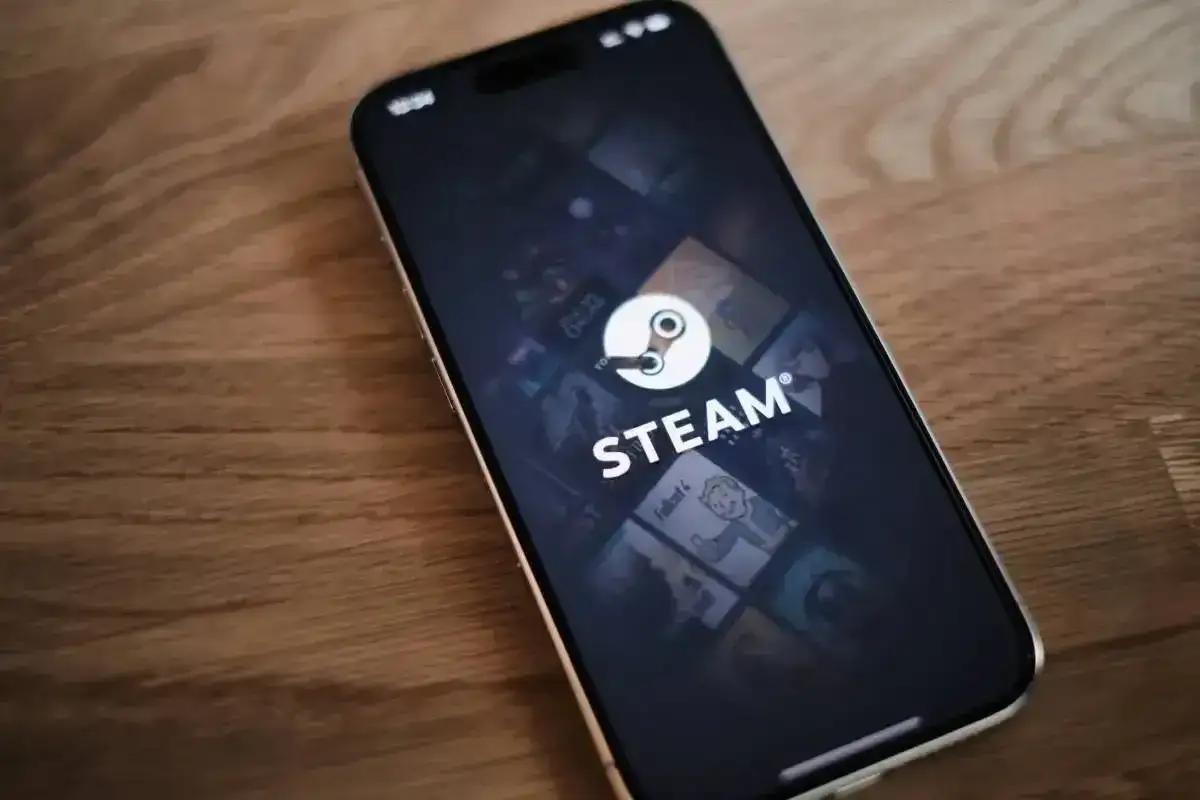 Telefon z aplikacją Steam, gdzie widać logo i okładki gier. W tle delikatna **steam cloud** unosząca się nad ekranem.