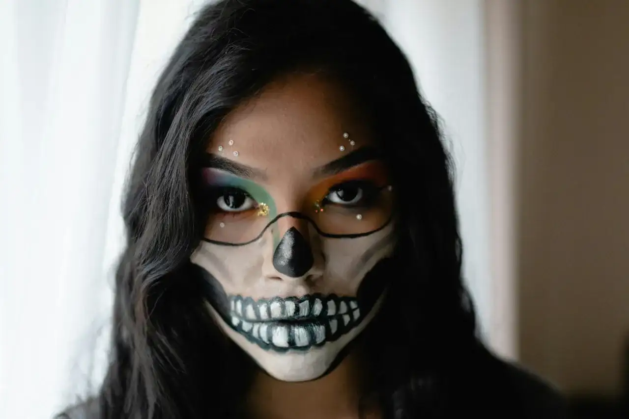 Makijaż na Halloween w stylu sugar skull: czarne kontury czaszki, kolorowe cienie do powiek i błyszczące dżety.