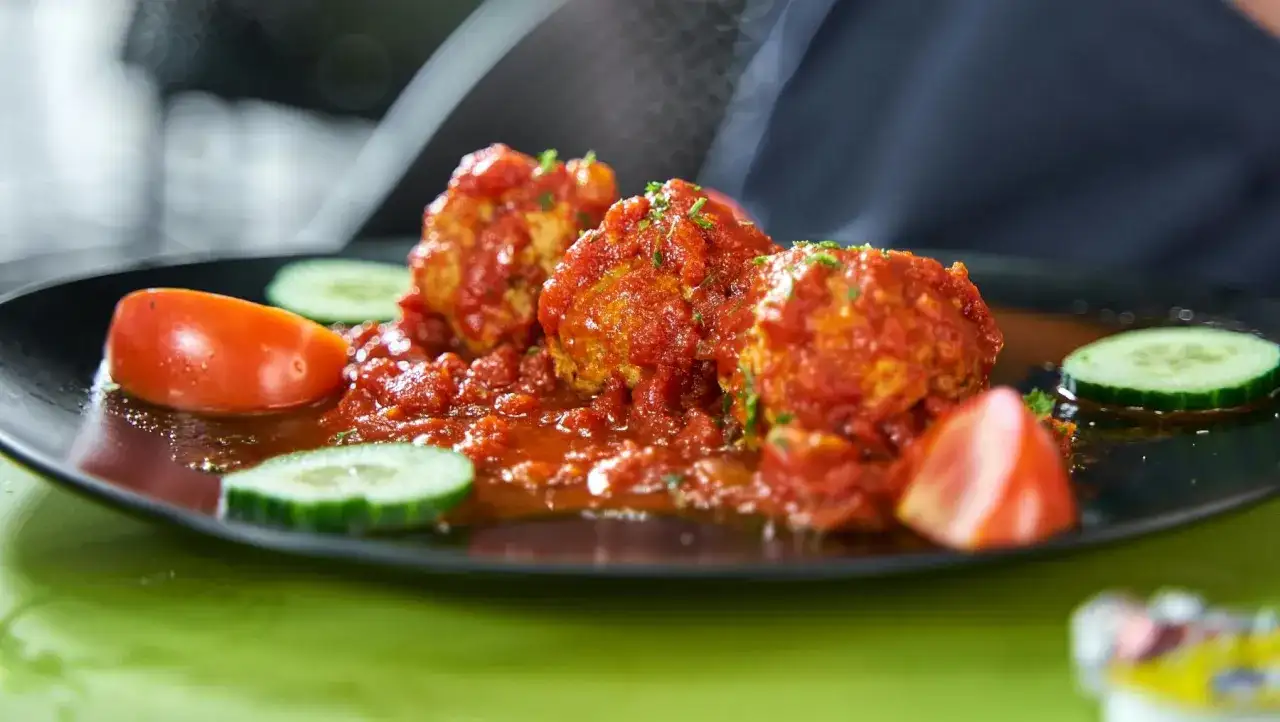 Albondigas con tomate, jugosas y cubiertas de salsa roja, acompañadas de rodajas de pepino y tomate fresco.