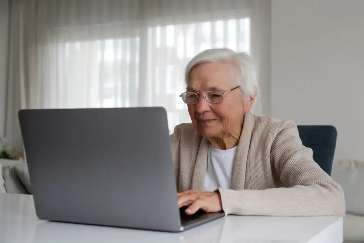 Uśmiechnięta starsza pani z okularami pracuje na laptopie, planując swoją emeryturę bez podatku.