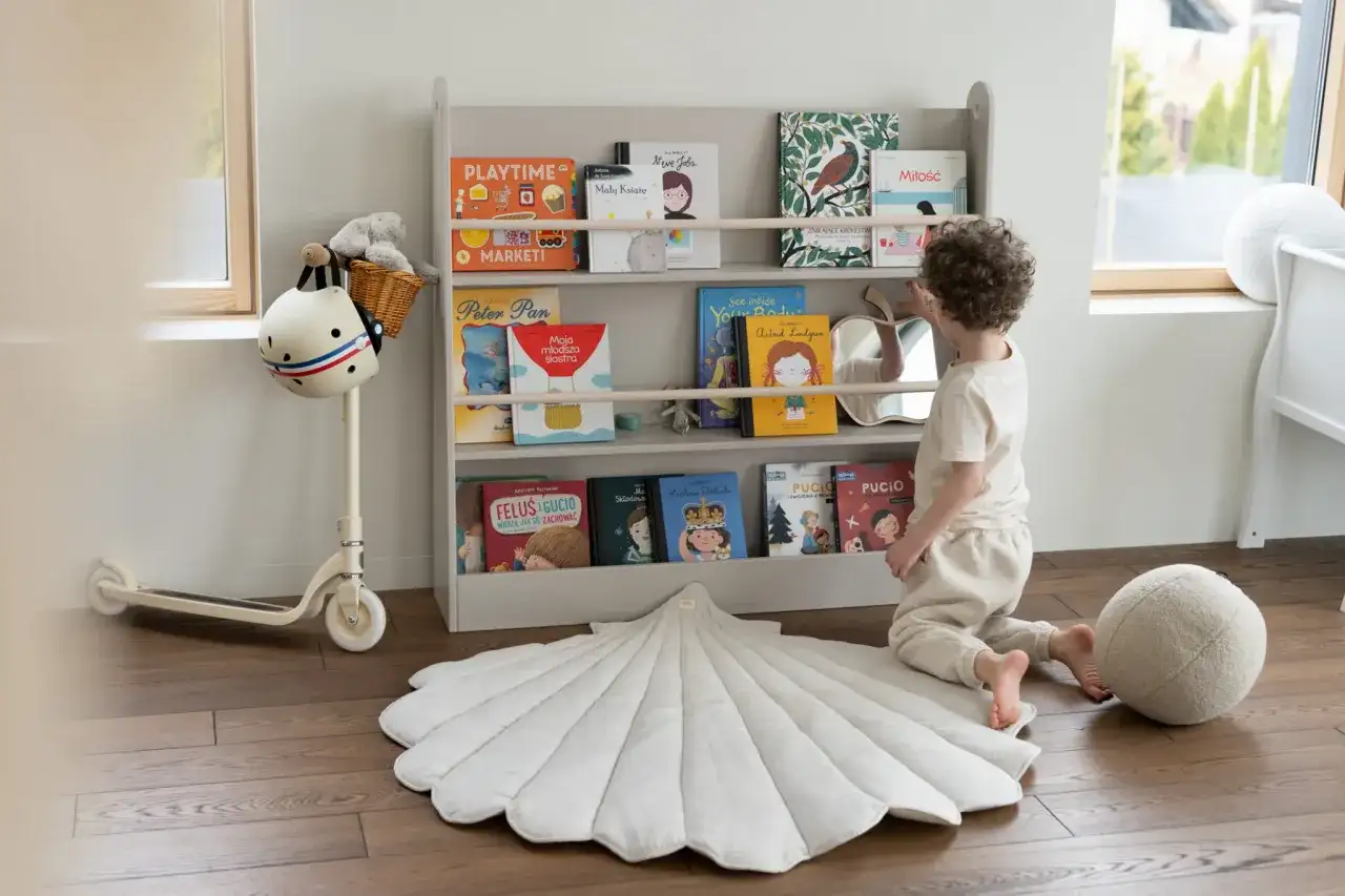 Chłopiec wybiera książkę z regału, tworząc przytulną przestrzeń do nauki i zabawy. Idealne miejsce na montessori w domu.